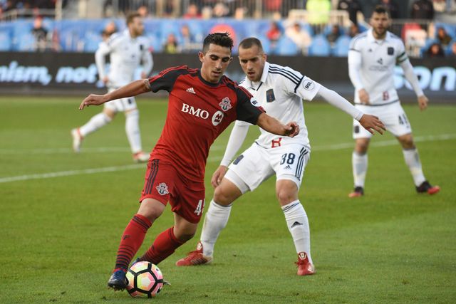 Luca in a red Toronto FC II #45 kit dribbling past an opponent in white.